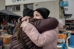 Zwei Frauen aus der Ukraine halten sich im Arm und stehen vor einem zerstörten Gebäude
