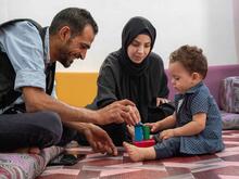 Anas, ein IRC-Freiwilliger, stärkt Familien in Jordanien und spielt mit einem Kleinkind und der Mutter.