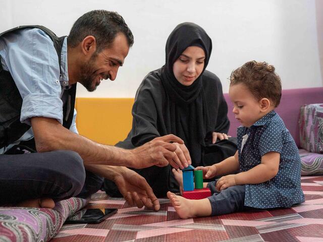 Anas, ein IRC-Freiwilliger, stärkt Familien in Jordanien und spielt mit einem Kleinkind und der Mutter.