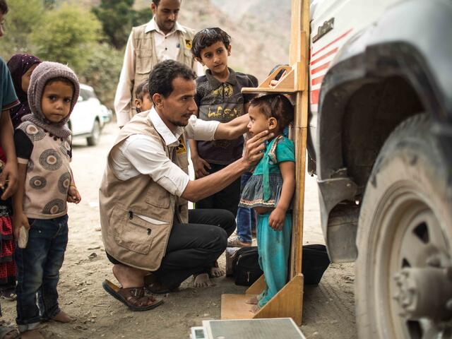 Ein IRC-Mitarbeiter misst einen kleinen Jungen im Bergdorf Okiba, Jemen. Andere Kinder schauen zu.