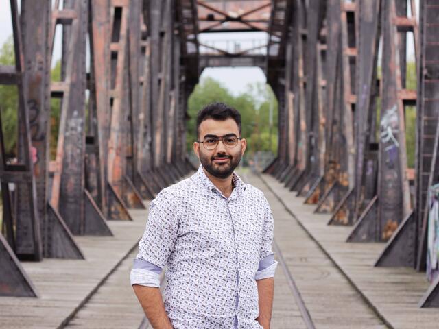 Zain, ein junger Mann steht auf einer Brücke in Magdeburg und lächelt in die Kamera.
