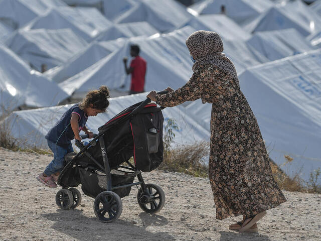 Eine Frau schiebt einen Kinderwagen mit ihrer Tochter durch ein Flüchtlingslager in Griechenland.