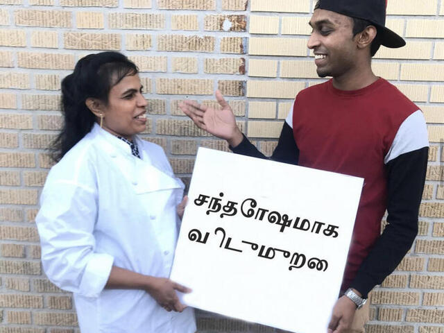 Mutter und Sohn mit Schild „Frohe Feiertage“ auf Tamil. 