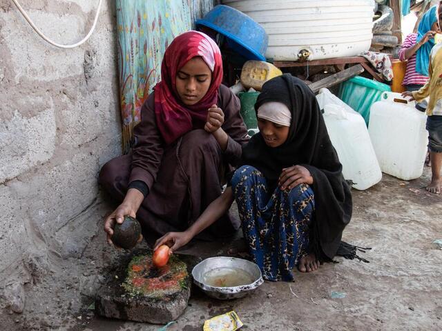 Zwei Mädchen hocken am Boden und bereiten Essen zu in Jemen.