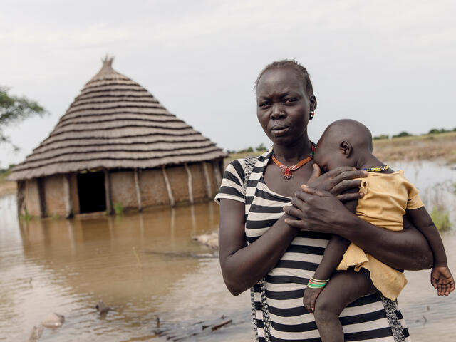 Eine Mutter hält ihr schlafendes Baby vor ihrem überfluteten Haus im Südsudan