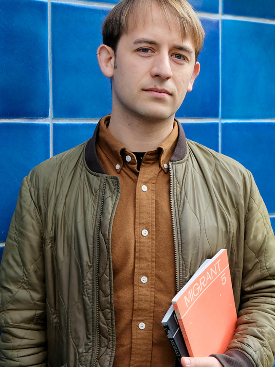 Ein Mann steht vor einer blauen Wand und hält ein Buch in der Hand