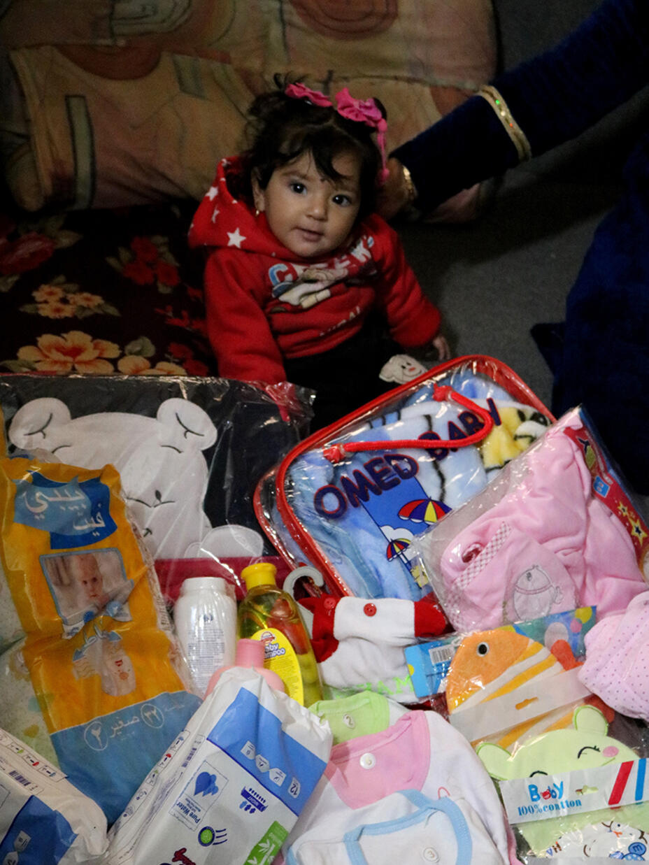 Baby im Areesha Flüchtlingslager sitzt zwischen dem Inhalt des Neugeborenen Pakets 
