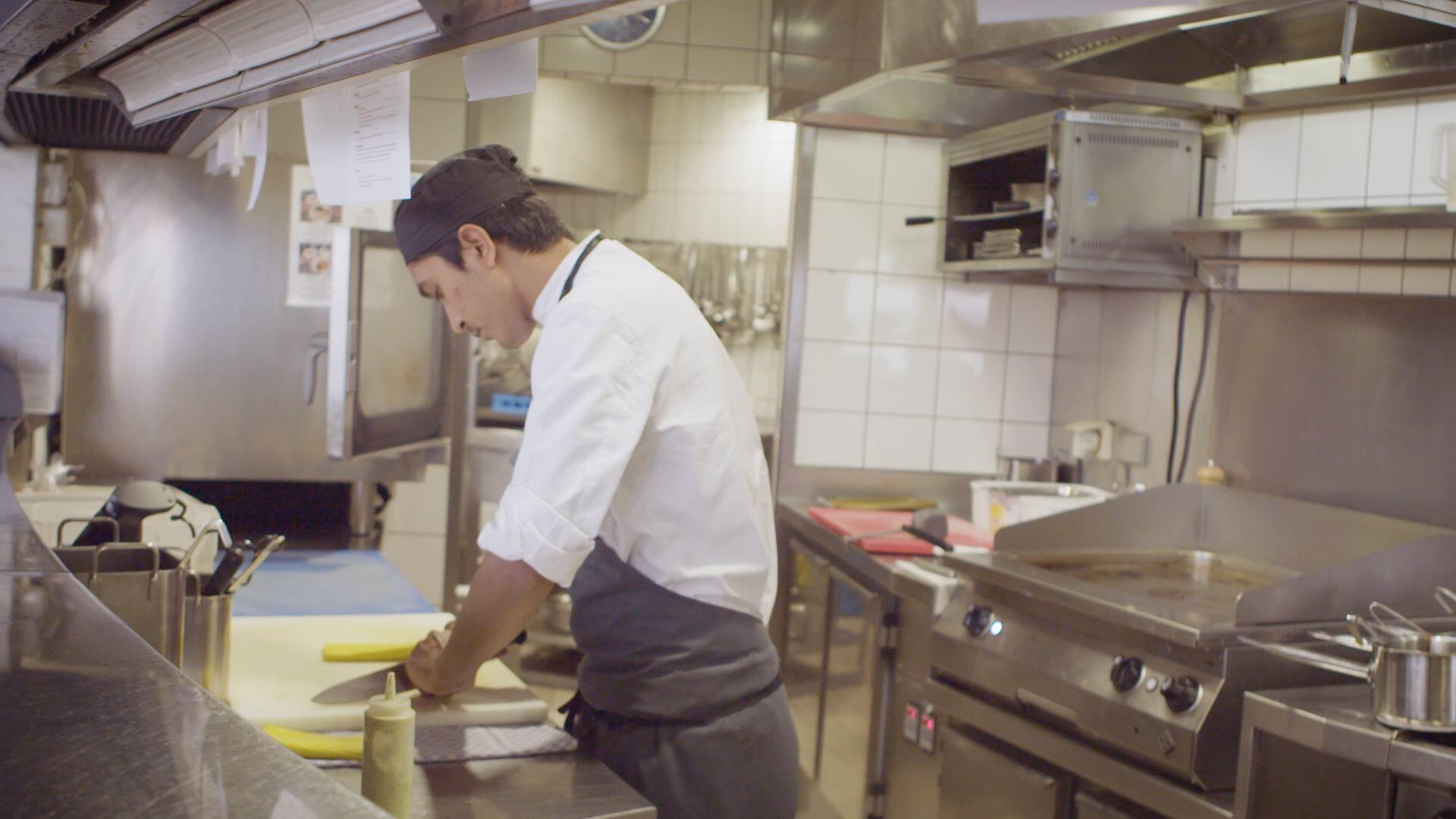 Ein junger Mann steht in einer professionellen Küche und bereitet Essen vor.