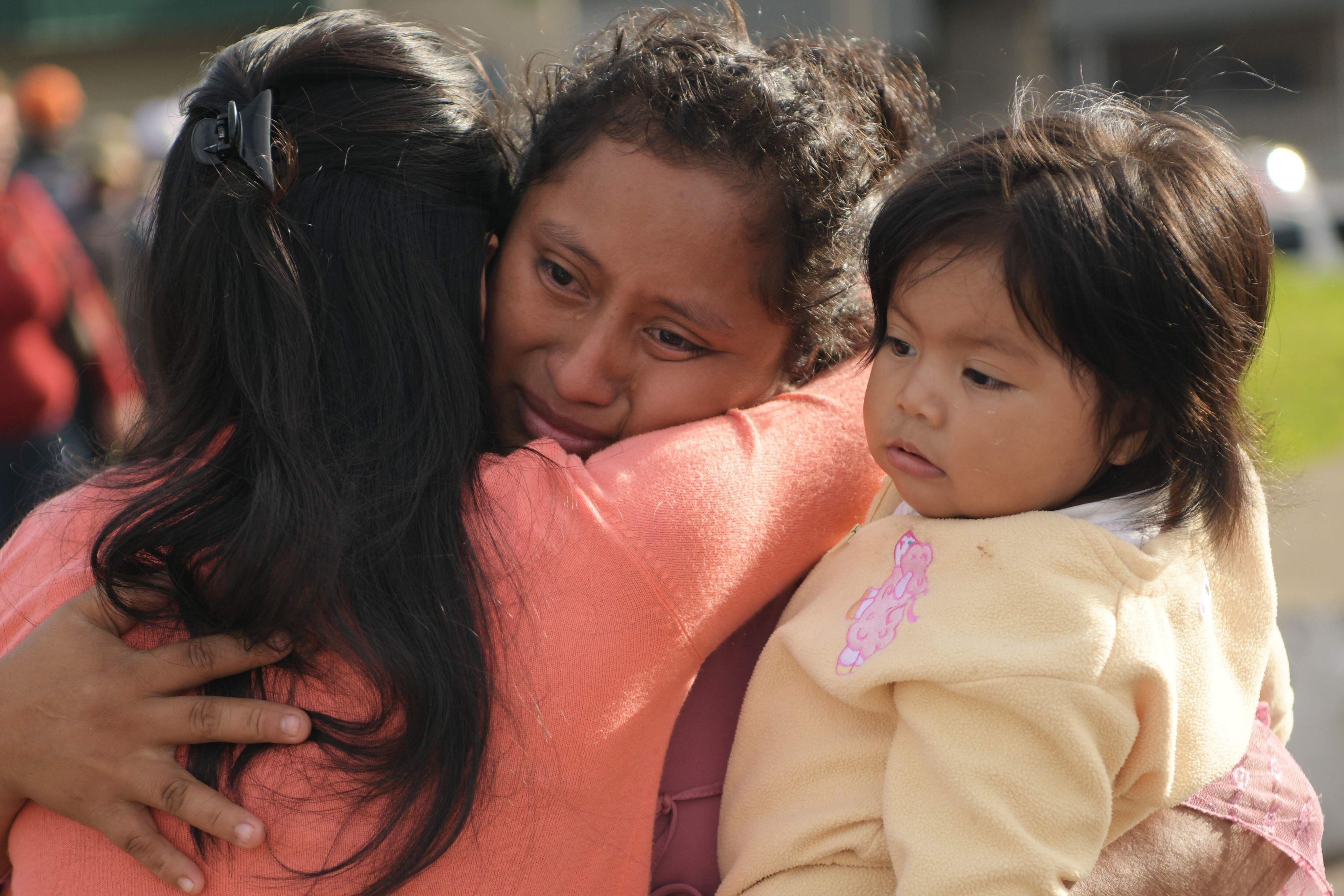 Eine Frau hält ein Kind im Arm, weint und umarmt eine andere Frau.