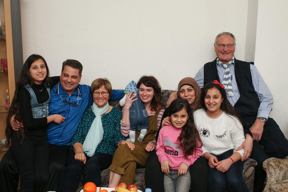 Viele Memschen sitzen auf einem Sofa und alle lächeln in die Kamera