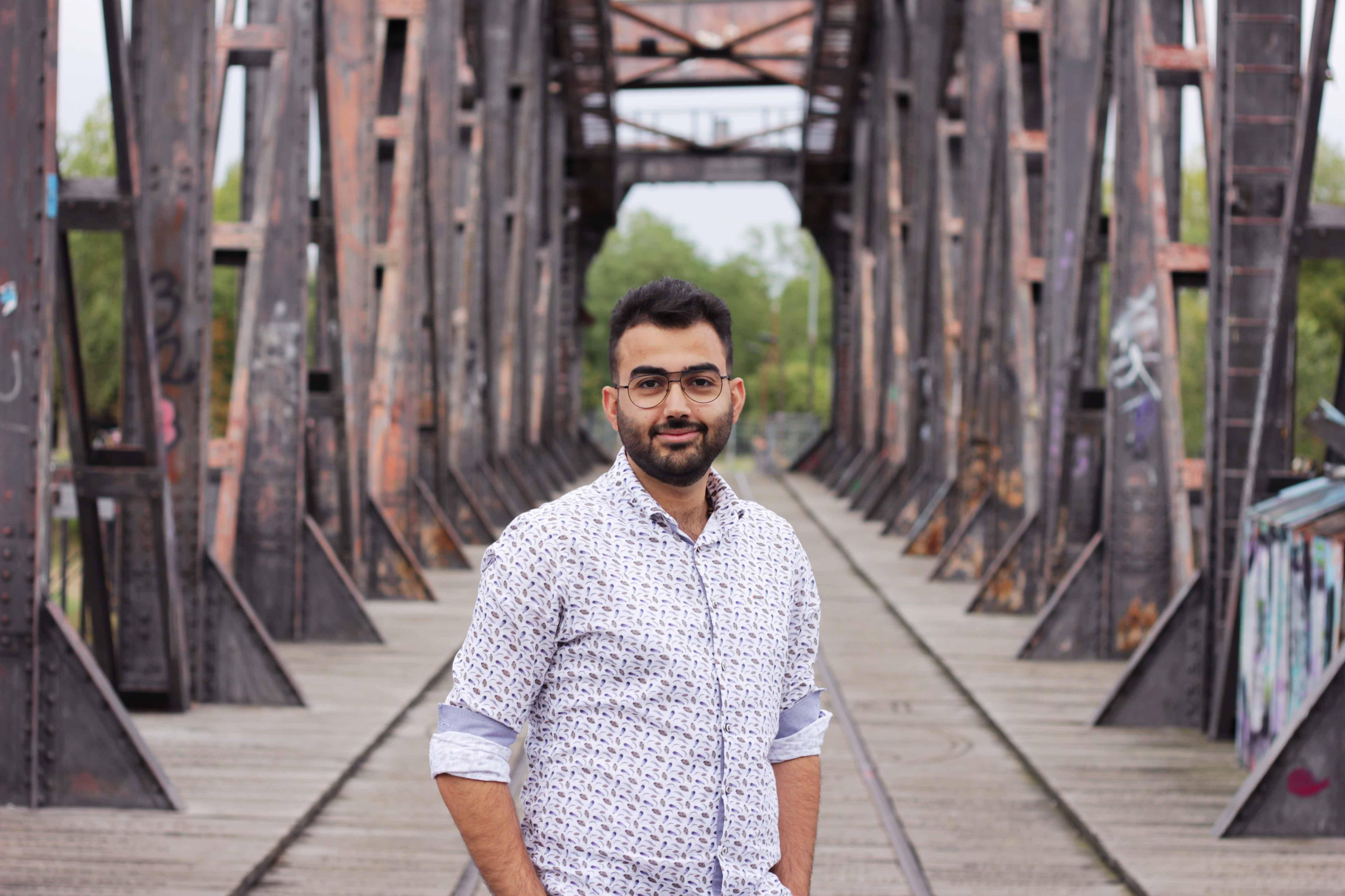 Zain, ein junger Mann steht auf einer Brücke in Magdeburg und lächelt in die Kamera.