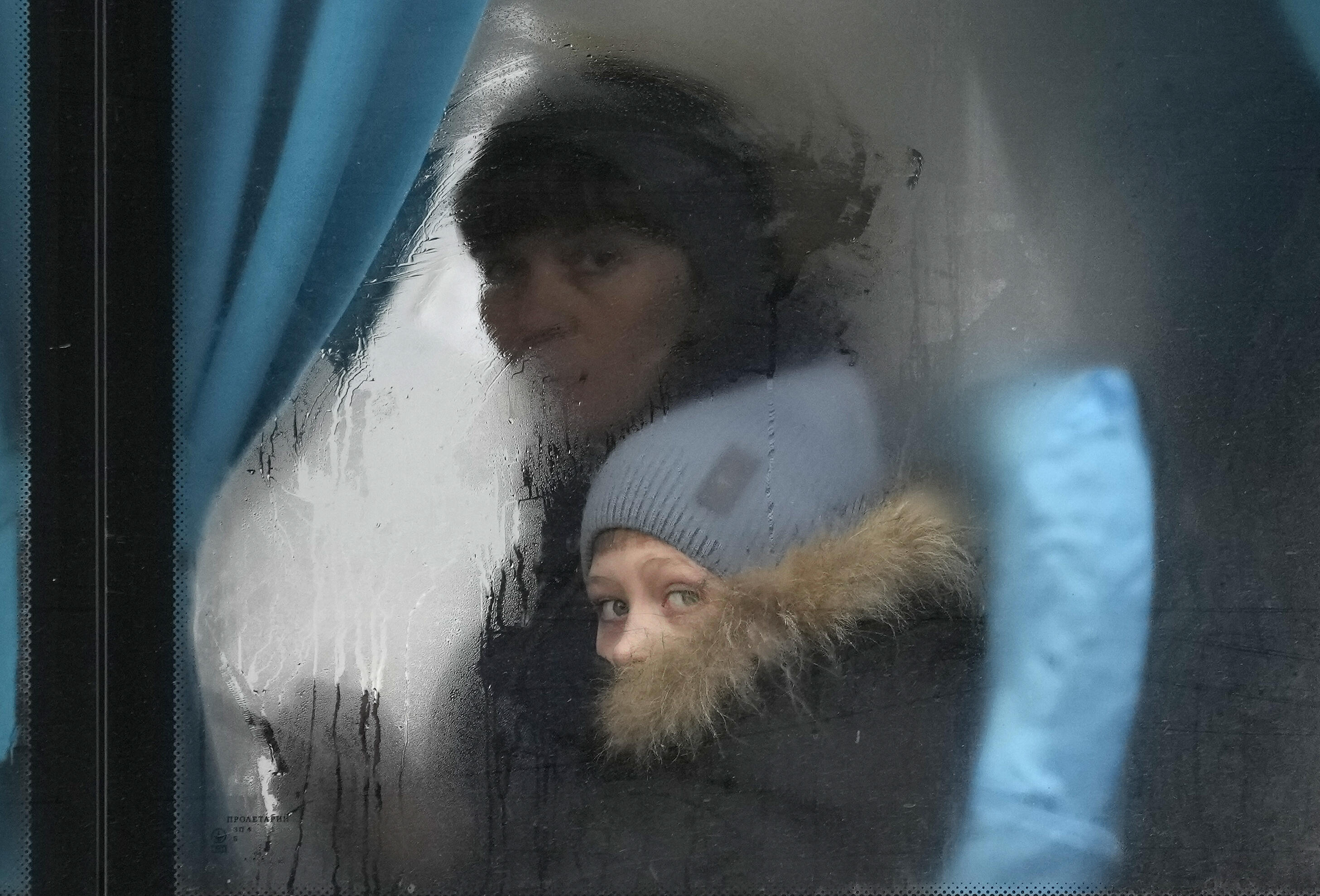 Eine Frau und ihr Sohn sitzen in einem Bus und gucken raus in die Kamera