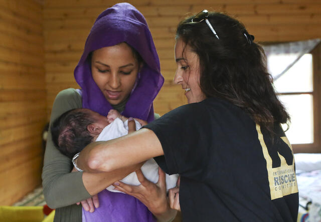Eine Frau mit Kopftuch hält ein Baby, eine zweite Frau hilft ihr.