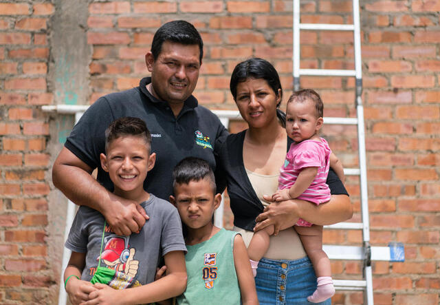 Eine venezuelanische Familie steht vor einer Mauer und eine Leiter steht im Hintergrund
