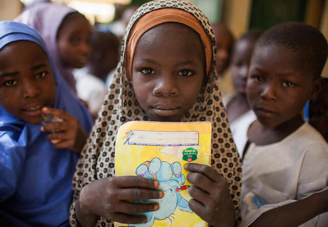 Ein Mädchen hält ein Schulbuch in der Hand und lächelt in die Kamera