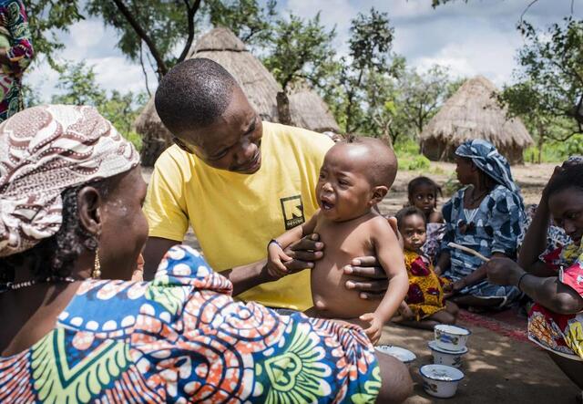 ein Gesundeheitshelfer von IRC hält ein unterernährtes Kleinkind in seinem Arm