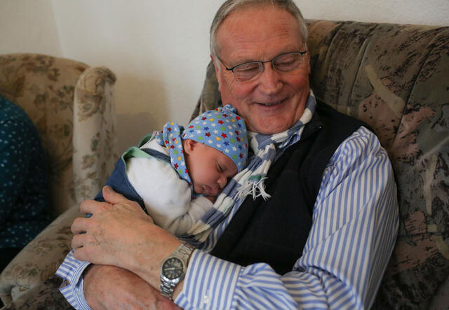 Ein alter Mann hält ein kleines Baby im Arm und lächelt