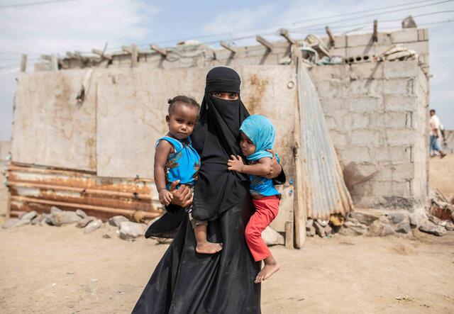 Eine vertriebene Frau steht mit ihren beiden Kindern im Arm vor einem Haus in Aden, Jemen