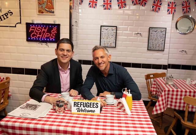 David Miliband und Gary Lineker sitzen lachend an einem Tisch mit karierter Tischdecke.
