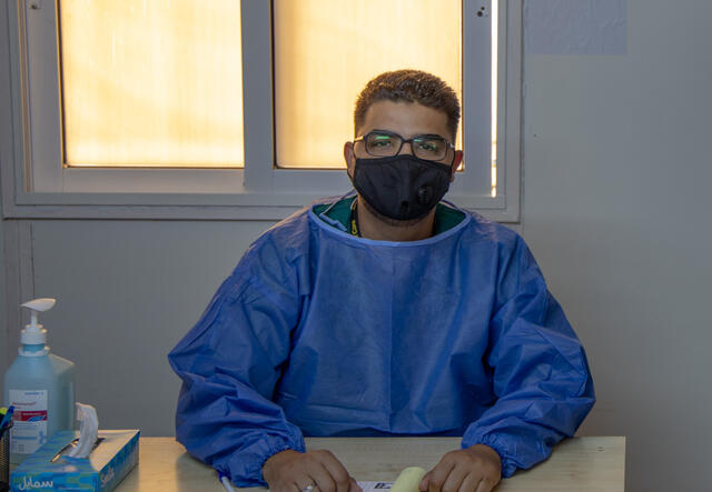 Dr. Abedalhaleem Albalasmeh sitzt mit Maske und Schutzkleidung an einem Schreibtisch.