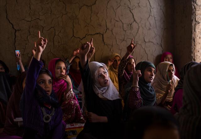 Eine Gruppe von Mädchen in Afghanistan sitzt im Unterricht. Die Mädchen haben ihr Hand erhoben und beteiligen sich an der Schul-stunde