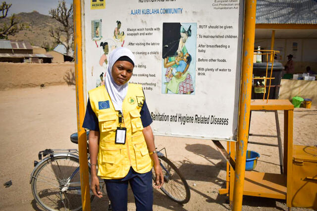 Aishatu vor einem Info-Schild an ihrem Arbeitsplatz in Nigeria