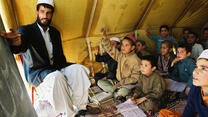Ein Lehrer unterrichtet in einem Zelt, seine Schüler sitzen auf einem Teppich.