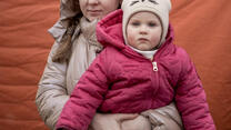 Iryna hält ihr Kind im Arm während beide in die Kamera schauen und Winterbekleideung tragen 