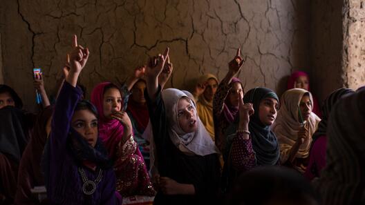 Eine Gruppe von Mädchen in Afghanistan sitzt im Unterricht. Die Mädchen haben ihr Hand erhoben und beteiligen sich an der Schul-stunde